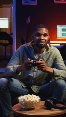 Dikey Video POV genç siyahi yetişkin akıllı TV 'de atış oyunu oynayarak, oturma odasında konsol takarak ve geceleri oyun oynayarak eğleniyor. Eğlenceli aktiviteler yapan bir adam. Kamera.