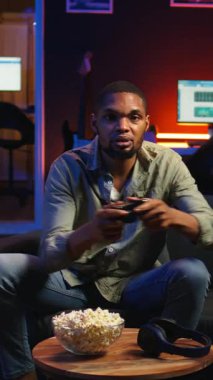 Evde boş zamanlarında video oyunlarıyla eğlenen, çevrimiçi atış turnuvasındayken patlamış mısır yiyen dikey video oyuncusu. Gevşemiş adam atıştırmalıklar ve yarışmayla oyun gecesinin tadını çıkarıyor.