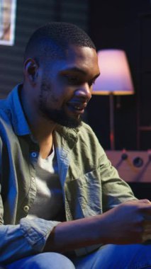 Dikey Videolu Dertsiz Serbest Çalışan telefonda arkadaşlarıyla mesajlaşır, kanepede oturur ve sosyal medya uygulamalarını kaydırır. Siyahi adam çalışırken eğleniyor.