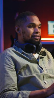 Dikey Video Siyah, görevlerini tamamlamak için kulaklıklara odaklanmış müzik dinliyor. Oturma odasında fasulye torbasında birden fazla iş yapıyor. Sakin çalışmanın keyfini çıkaran genç yetişkinler görevlerini tamamlamak için seslerini çıkarıyorlar.