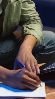 Dikey Video Siyah Serbest Çalışan, ödevlerini çözmek, araştırma yapmak ve makaleleri çevrimiçi okumak için ders kitabı üzerine notlar alıyor. Uzaktan kumandalı işten ve gevşek programdan hoşlanan genç yetişkinler.