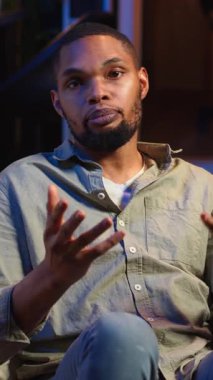 Evdeki bir video görüşmesi sırasında gülümseyen ve sohbet eden dikey Afrikalı Amerikalı kişi, görevleri tamamlamak için görüşlerini web buluşmasındaki meslektaşlarıyla paylaşıyor. Dijital ve kablosuz yaşam tarzı. Kamera B.