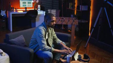 Şık bir oturma odasında dizüstü bilgisayarıyla telgraf çeken odaklanmış Afrikalı Amerikalı bir adam. Modern bir çalışma alanında konfor ve verimliliği dengeleyen uzaktan kumandalı bir işçi. Rahat bir çatı katı stüdyosu. Kamera A.