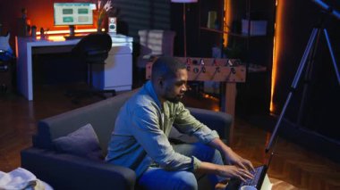 İnternette yayınlanan bir yayını dinleyen Afrikalı Amerikalı serbest yazar oturma odasındaki kanepede otururken kulaklık takıyor. Sıradan bir evde birden fazla iş. Kamera A.