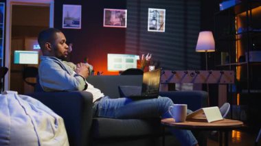 Sanal toplantı sırasında iş arkadaşlarına el sallayan, online araçların etkinliğini ve internet bağlantısını gösteren uzaktan çalışan bir erkek. Bir brifing oturumunda genç bir yetişkin görüşünü paylaşıyor. Kamera A.