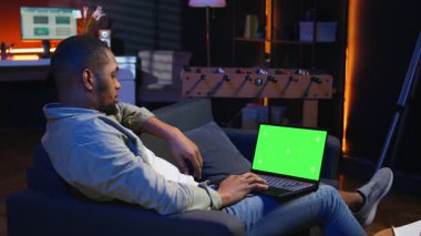 Afrikalı Amerikalı uzaktan kumandalı işçi oturma odasında çalışmak için krom anahtar ekranı kullanıyor, modern şık oturma odasındaki kanepede oturuyor. İnternetteki genç mutlu yetişkin. Kamera A.