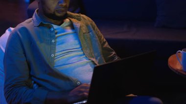 Yetişkin bir adam evdeki fasulye torbasının üzerine yatarken bilgisayarında daktilo yazıyor. Serbest ve çevrimiçi işler yapıyor. Siyahi adam birden fazla iş yapıyor ve uzaktan kumandanın esnekliğini kucaklıyor. Kamera B.