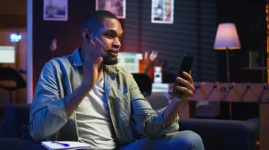 Evde cep telefonuyla video görüşmesinden keyif alan serbest çalışan, ders kitabına not alan ve önemli detaylar alan sakin bir adam. Konforlu oturma odası gösterileri, uzak yaşam tarzında iş ve eğlence. Kamera A.