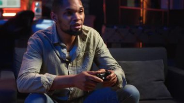Afrikalı Amerikalı adam boş zamanlarını patlamış mısırla oyun oynayarak geçiriyor. Oyun gecelerinde evinde eğleniyor. Genç yetişkin, konsolunu televizyona bağlıyor. Kamera B.
