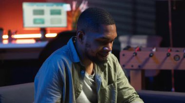 Afro-amerikalı bir insan koltukta akıllı telefon uygulaması üzerinden mesaj atıyor, evde dinlenmeden önce görevlerini tamamlıyor. Genç yetişkin cep telefonunu kaydırıyor, mesajlarla sohbet ediyor. Kamera B.