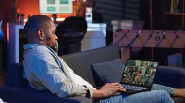 Kendine güvenen erkek konuşmacı web sitesindeki bir video konferans toplantısında iş arkadaşlarını selamlıyor, rahat çatı katında çevrimiçi uzaktan iletişimin faydalarından faydalanıyor. Siyah adam sanal tartışma sunuyor. Kamera B.