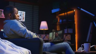 Oturma odasında bir web konferansı sırasında gülümseyen ve el sallayan, dijital ve kablosuz bir yaşam tarzında online tartışmalar yapan odaklanmış siyahi bir adam. Konferans konuşmacısı ve nöbetçi katılımcılar. Kamera A.