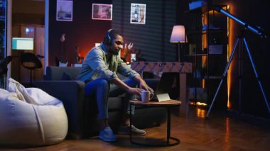 Dizüstü bilgisayarda çalışan Afrikalı Amerikalı adam neon ışıkların altında başarıyı kutluyor, rahat bir dairede kanepede oturuyor. Rahatlamış insan müzik dinler, görevlerinin başarısından memnundur. Kamera A.