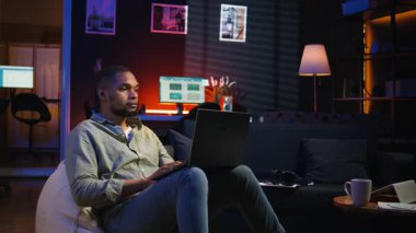 Modern çatı katından dizüstü bilgisayarla uzaktan kumandayla çalışan Afro-Amerikalı bir adam, bir fasulye torbasının üzerine uzanmış vazifelerini tamamlamaya odaklanıyor. Üretkenlik ve rahatlama ile telgrafı harmanlamak. Kamera A.