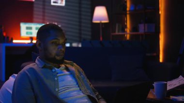 Siyahi adam oturma odasından bilgisayarla uzaktan kumanda yapıyor, ekrandaki çevrimiçi verileri kontrol ediyor. İş gelirlerini analiz eden ve karşılaştıran bir telgraf işçisi, geceleri odaklanıyor. Kamera A.