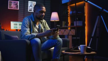 Rahat takılan, cep telefonuyla kanepede dinlenen, sosyal medyada arkadaşlarına mesaj atan ve gülen bir adam. Konforlu oturma odası gösterileri, uzak yaşam tarzında iş ve eğlence. Kamera A.