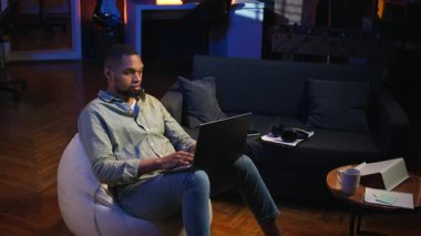 Siyah adam evde akıllı telefonunu kaydırarak işe ara veriyor, sosyal medyada arkadaşlarına mesaj atıyor ve eğleniyor. Neon ışıkları olan şık bir oturma odasında dinlenen adam. Kamera A.