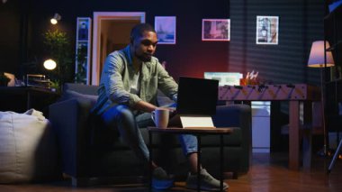 İnternette gezinen, müzik dinleyen, kulaklıktaki şarkılarla eğlenen ve görevleri tamamlayan serbest çalışan bir adam. Afro-Amerikalı adam kanepede uzanıyor ve oturma odasında dinleniyor. Kamera A.