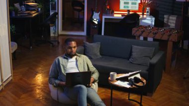 Genç siyahi biri dizüstü bilgisayarında uzaktan kumandalı bir video ile evde oturuyor, görevleri çözmek için online bir konferans web sitesine katılıyor. Oturma odasında telekonferans. Kamera A.