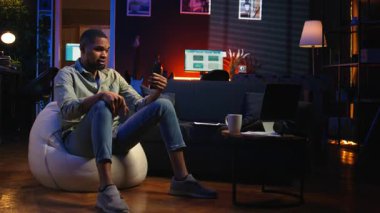 Afrikalı Amerikalı adam evde oturup bilgisayarla konferans görüşmelerine katılıyor. Günlük işleri çözmek için uzaktan kumandalı bir Webinar 'a katılıyor. Oturma odasında telekonferans. Kamera A.