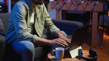 Şık bir oturma odasında dizüstü bilgisayarıyla telgraf çeken odaklanmış Afrikalı Amerikalı bir adam. Modern bir çalışma alanında konfor ve verimliliği dengeleyen uzaktan kumandalı bir işçi. Rahat bir çatı katı stüdyosu. Kamera B.