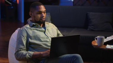 Ürün ve hizmetler hakkında stratejik tavsiyelerde bulunmak için aylık bütçeyi ve harcamaları inceleyen analist. Zenci genç iş adamı gelir dengesi analizi yapıyor, evde muhasebe yapıyor. Kamera B.