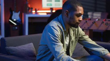 İnternette yayınlanan bir yayını dinleyen Afrikalı Amerikalı serbest yazar oturma odasındaki kanepede otururken kulaklık takıyor. Sıradan bir evde birden fazla iş. Kamera B.