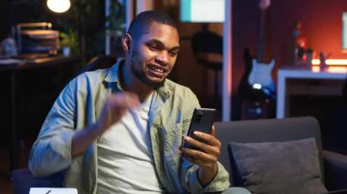 Afrikalı Amerikalı tele-işçi video konferansında iş arkadaşını arayıp notlar alıyor, yeni fikirler yazıyor ve oturma odasında internet görüşmeleri hakkında bilgi alışverişinde bulunuyor. Ders kitabı verileri. Kamera B.