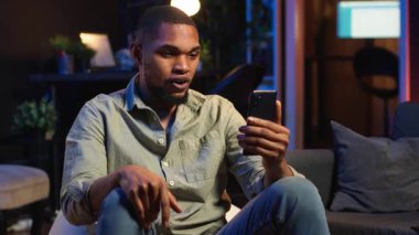 Afrikalı Amerikalı adam evde oturup bilgisayarla konferans görüşmelerine katılıyor. Günlük işleri çözmek için uzaktan kumandalı bir Webinar 'a katılıyor. Oturma odasında telekonferans. Kamera B.