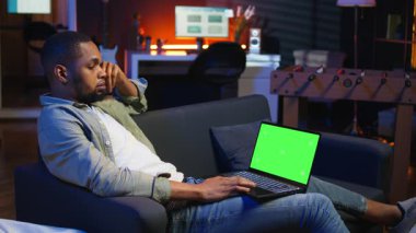 Oturma odasındaki izole edilmiş fotokopi odasını kullanan, modern oturma odasındaki kanepesinde neon ışıkları ve son moda mobilyalarla süslenmiş kendine güvenen genç bir serbest yazar. Elinde aletler olan adam. Kamera A.