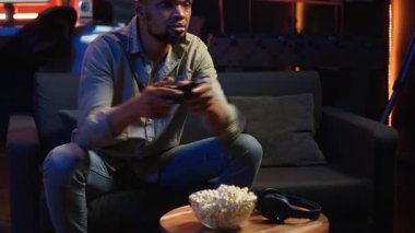 Erkek oyuncu online atış turnuvasındayken patlamış mısır yiyor, evdeki boş zamanlarında video oyunlarıyla eğleniyor. Gevşemiş adam atıştırmalık ve rekabetle oyun gecesinin tadını çıkarıyor. Kamera B.