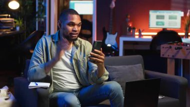 Evde cep telefonuyla video görüşmesinden keyif alan serbest çalışan, ders kitabına not alan ve önemli detaylar alan sakin bir adam. Konforlu oturma odası gösterileri, uzak yaşam tarzında iş ve eğlence. Kamera B.