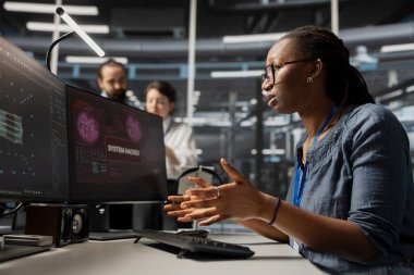 Veri merkezindeki korkmuş yönetici virüs alarmı yüzünden panikledi ve kritik sistemleri korumak için protokolü başlattı. Sunucu odasında Afrikalı Amerikalı bir kadın hacker saldırısından sonra tehlikeli teçhizat değerlendirmesi yapıyor.