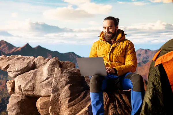 Dağ maceracısı, aşırı rüzgara rağmen dizüstü bilgisayarı üzerinde çalışarak çevrimiçi işini güvenlikten üstün tutuyor. Nefes kesen manzara, internet bağımlılığıyla gölgeleniyor..
