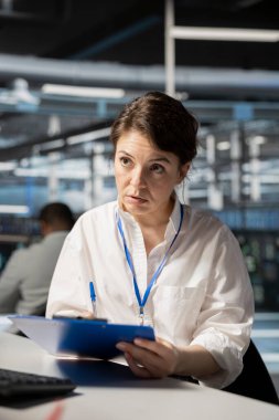 Sunucu odası yöneticisi planlanan denetimden önce panodaki belgeleri inceliyor. Yapılandırma verisi ve uyum standartlarını masadan doğrulayan veri merkezi yönetimi