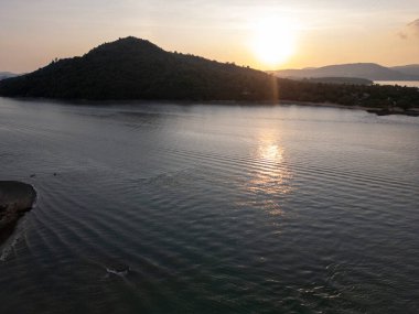 Yelkenli tekneler ve yemyeşil ada manzaralı tropikal körfezin insansız hava aracı görüntüleri, limanı ve berrak mavi suları olan sakin kayalık bir sahile sahip güzel deniz manzarası. Egzotik kıyı manzarası.