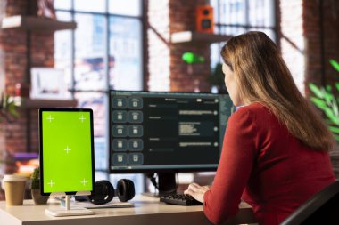 Kişi, yeşil ekranın yanındaki web arayüzünde uzaktan kumanda ile dijital yapay zeka aracı kullanır. Yapay zeka destekli arayüz iletişimi basitleştirir ve verimliliği artırır.