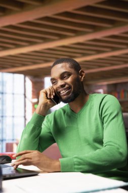 Evde gülümseyen bir adam akıllı telefondan arkadaşlarıyla dostça sohbet ediyor. Afro-amerikalı bir insan telefonda arkadaşlarıyla eğleniyor, canlı sohbetler ediyor.
