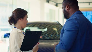 Satış temsilcisi müşteriyle konuşuyor, tercihlerini, ilgi alanlarını ve vücut dillerini gözlemliyor ve onların satın alma kararlarını neyin etkileyebileceğini kavrayabilmek için not alıyor.