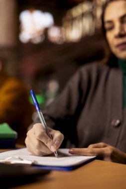 Yetişkin öğrenci, akademik ders kitapları ve arşivlenmiş belgelerle çevrili bir üniversite kütüphanesinde ders sırasında bilgi yazar. Yüksek öğrenim kampüsündeki kişisel hedefler. Kapat..