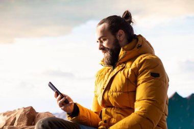 Doğa aşığı dağın tepesinde rahatlıyor telefonuyla manzaraya bakan manzaralı bir bakış açısıyla internete giriyor. Yürüyüşçü her zaman çevrim içi ve bağlı kalıyor, panoramik manzara.