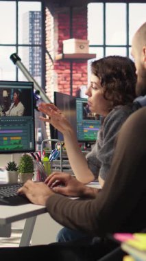 Vertical Video Man ve kadın film yapımcıları, yaratıcı bir video projesi için modern teknoloji kurulumu ve kurgu yazılımı kullanarak, post prodüksiyon videolarında video çekimleri düzenliyorlar. Çift monitörlü modern çalışma alanı. Kamera A