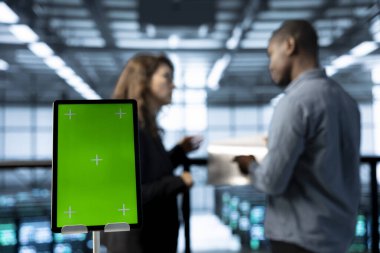 Otomasyon araçları kullanarak veri merkezindeki işçilerin yanındaki tableti kapat. Sunucu çiftliğinin sürekli güncellenmesini sağlayan bulanık arkaplandaki teknisyenlerin önündeki izole ekran tabletine odaklan