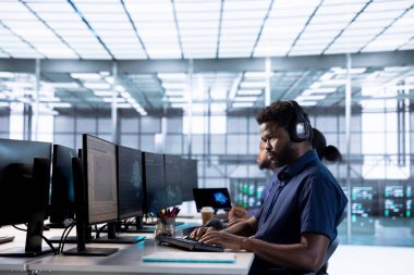 Yüksek işlemci kullanımı nedeniyle sunucu performans sorunları için PC 'yi kullanırken veri merkezinde müzik dinleyen bir mühendis. Sunucu çiftliğinde kulaklık takan adam yetersiz hafıza hatalarını düzeltiyor