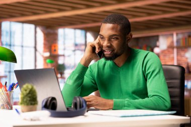 Neşeli bir adam telefon görüşmesi sırasında arkadaşlarıyla dostça sohbet ediyor. Gülümseyen Afrikalı Amerikalı arkadaşlarıyla eğleniyor, telefonda konuşuyor.