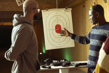 Atış poligonu güvenliği müşterilerin güvenle çalışmasını sağlıyor. Atış poligonu çalışanı yarı otomatik silahlara izin vermeden önce müşterilerle kuralları tartışıyor.