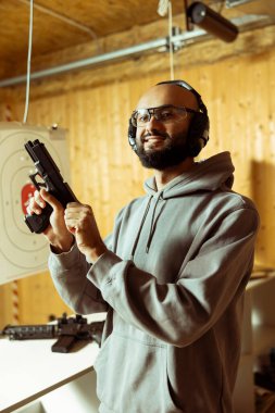 Atış poligonunda silah taşıyan mutlu bir Arap 'ın portresi, ateş etmek için mekanizma kuruyor. Neşeli Orta Doğulu antrenman sırasında tabanca çekiçini çekip ateş etmeye hazırlanıyor.