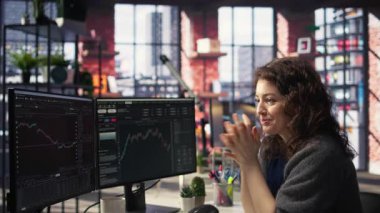 Heyecanlı kadın borsa analizinde çalışıyor. Monitörlerindeki gerçek zamanlı verileri inceliyor. Dijital platformda mali istatistikler, önx eğilimleri ve yatırım anlayışları yer alıyor. Kamera A.