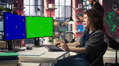 Profesyonel kadın, modern çalışma alanında çift ekran monitörlerde yeşil ekran kullanıyor. Yüksek teknoloji ofis ortamı üretkenliği, bilişim uzmanlarını ve içerik yaratmayı arttırır. Kamera A.