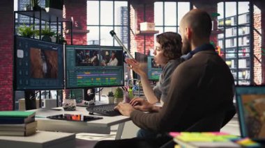Erkek ve kadın film yapımcıları, modern teknoloji kurulumu ve yaratıcı bir video projesi için kurgu yazılımı kullanarak, post prodüksiyonda video çekimleri düzenliyorlar. Çift monitörlü modern çalışma alanı. Kamera A.